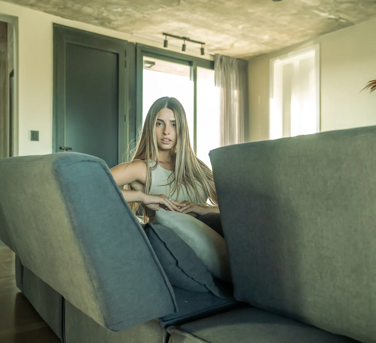 Mujer sentada en un sillón modular gris en un living con ventanales